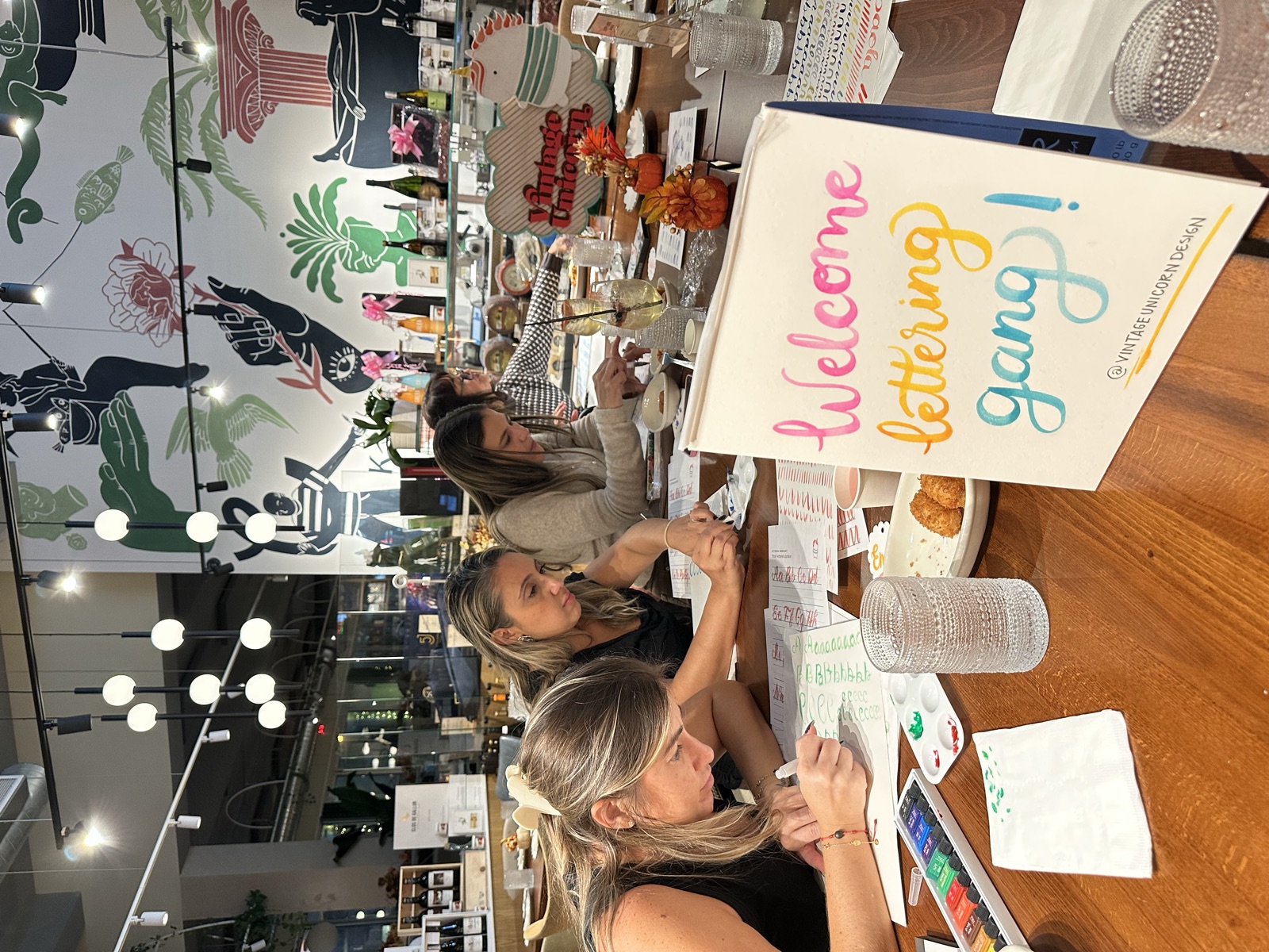 Beginners practicing watercolor brush lettering on worksheets at a long table at CalaMillor Gourmet Experience in Miami