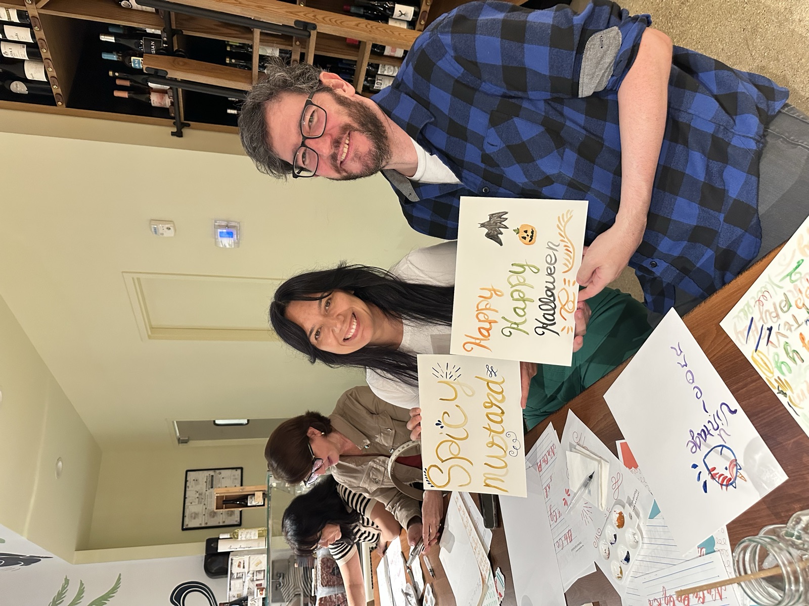 Two students showing their finished watercolor brush lettering pieces, including a Happy Halloween card, at a lettering workshop in Miami